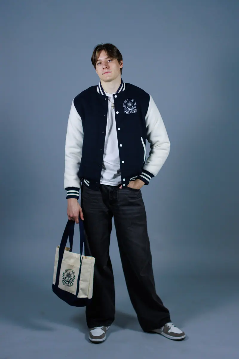 A student in a navy varsity jacket carrying a cream tote